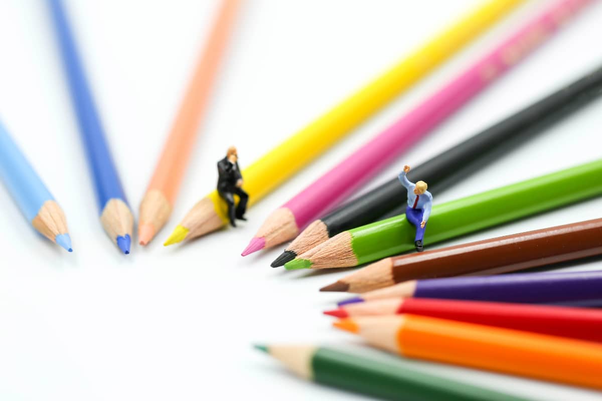 mini people sitting on colored pencils